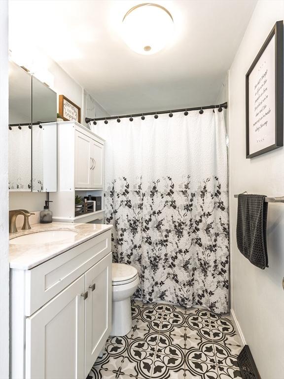 full bath featuring toilet, vanity, and curtained shower