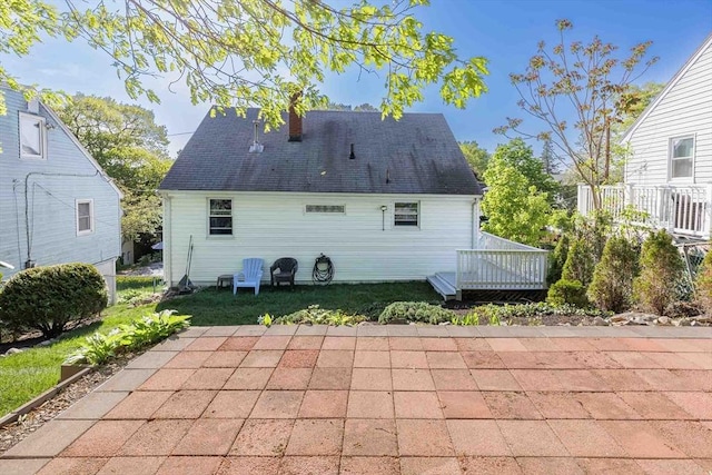 back of house featuring a deck, a chimney, a patio, and a shingled roof