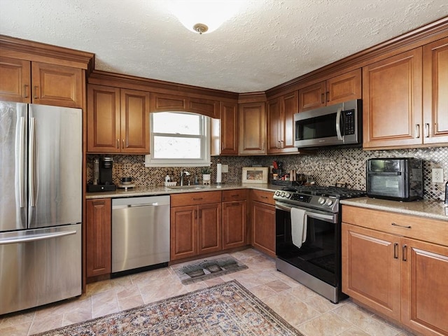 kitchen featuring stainless steel appliances, a sink, brown cabinetry, decorative backsplash, and a textured ceiling