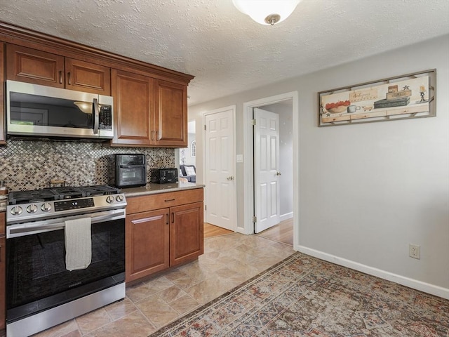 kitchen with appliances with stainless steel finishes, decorative backsplash, baseboards, brown cabinets, and a textured ceiling