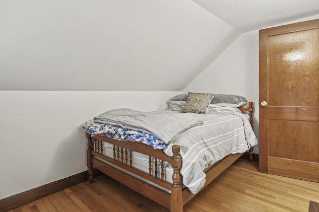 bedroom with baseboards, light wood-style flooring, and lofted ceiling