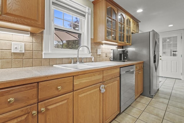 kitchen with stainless steel dishwasher, light tile patterned flooring, glass insert cabinets, light countertops, and a sink
