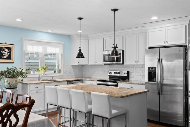 kitchen featuring white cabinetry, sink, decorative light fixtures, a kitchen island, and appliances with stainless steel finishes