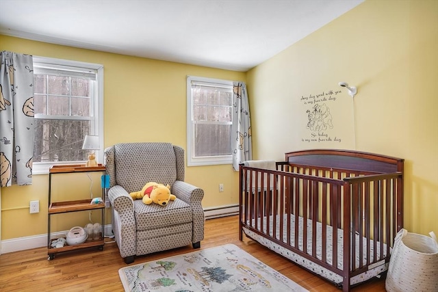 bedroom with a baseboard heating unit, multiple windows, wood finished floors, and baseboards