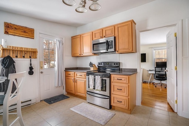 kitchen with light tile patterned floors, stainless steel appliances, baseboard heating, and dark countertops