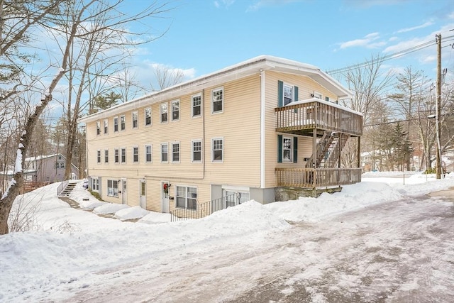 snow covered back of property featuring stairway and a wooden deck