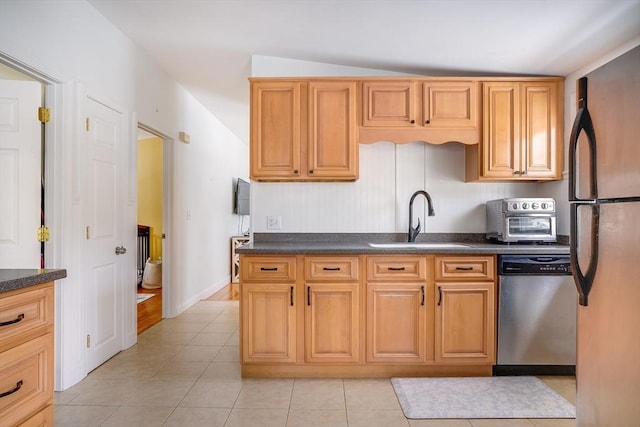 kitchen featuring light tile patterned floors, stainless steel appliances, dark countertops, and a sink