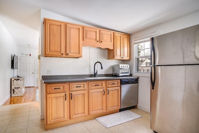 kitchen with dark countertops, stainless steel appliances, a sink, and light tile patterned flooring