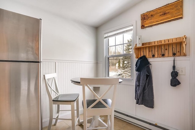 dining area featuring a baseboard heating unit, light tile patterned floors, and wainscoting