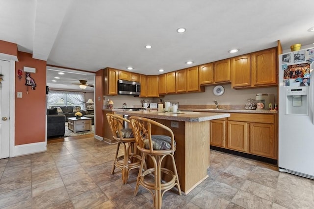 kitchen with ceiling fan, a kitchen island, a breakfast bar, sink, and white fridge with ice dispenser