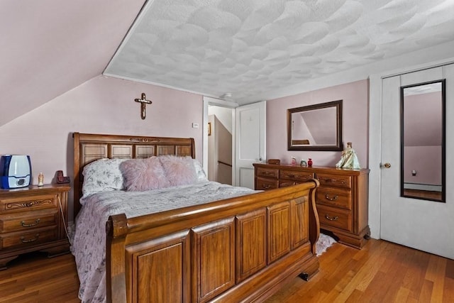 bedroom with lofted ceiling, a closet, a textured ceiling, and light hardwood / wood-style flooring