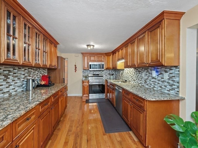 kitchen with light stone countertops, appliances with stainless steel finishes, backsplash, and light hardwood / wood-style flooring