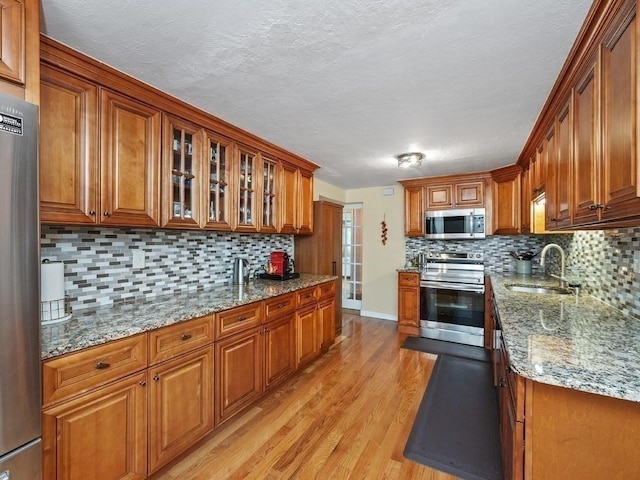 kitchen with light stone countertops, sink, stainless steel appliances, tasteful backsplash, and light hardwood / wood-style flooring