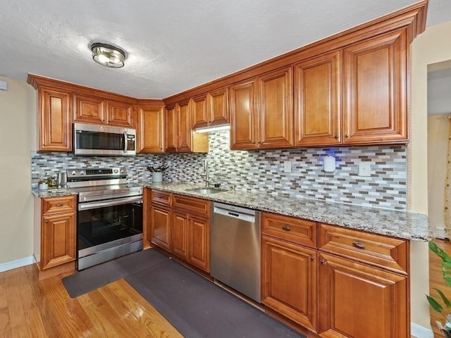 kitchen with sink, stainless steel appliances, tasteful backsplash, light stone counters, and dark hardwood / wood-style floors