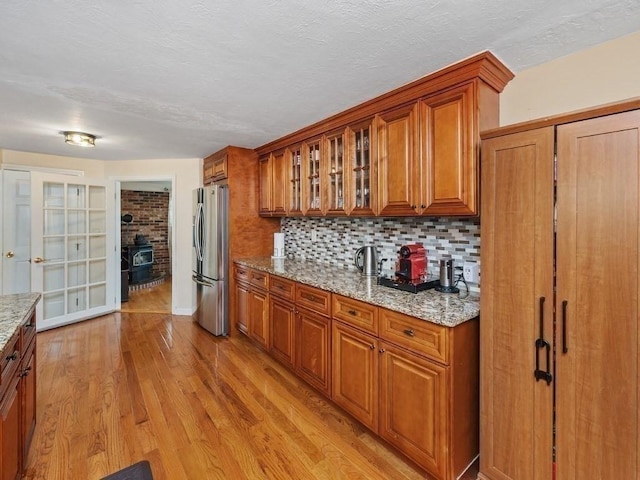 kitchen with a wood stove, light stone counters, backsplash, stainless steel fridge, and light wood-type flooring