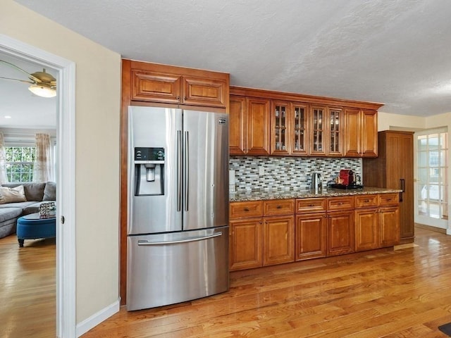 kitchen featuring stainless steel fridge, tasteful backsplash, light stone counters, ceiling fan, and light hardwood / wood-style flooring