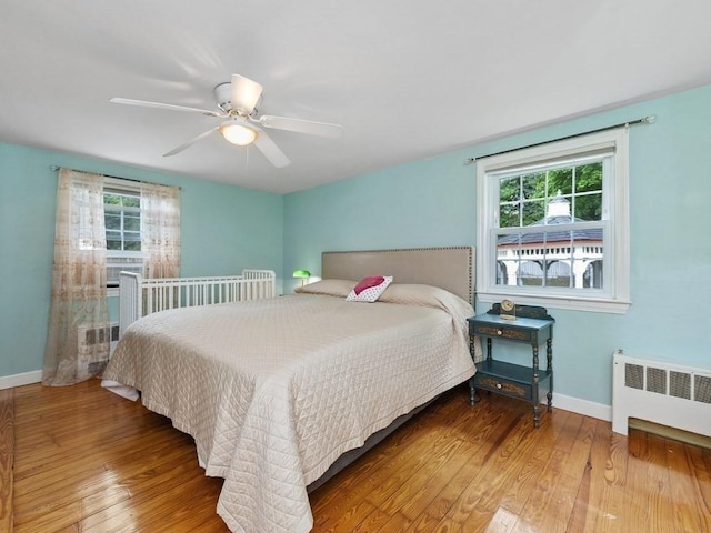 bedroom with multiple windows, wood-type flooring, radiator, and ceiling fan