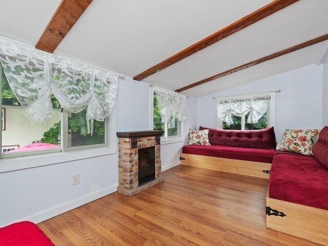 living room with hardwood / wood-style floors, vaulted ceiling with beams, and a stone fireplace