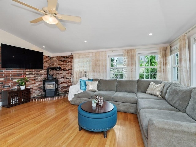 living room with brick wall, ceiling fan, wood-type flooring, a wood stove, and lofted ceiling