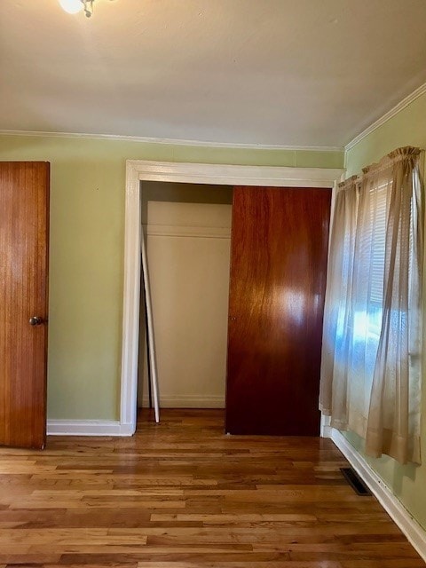 unfurnished bedroom featuring a closet, hardwood / wood-style floors, and crown molding