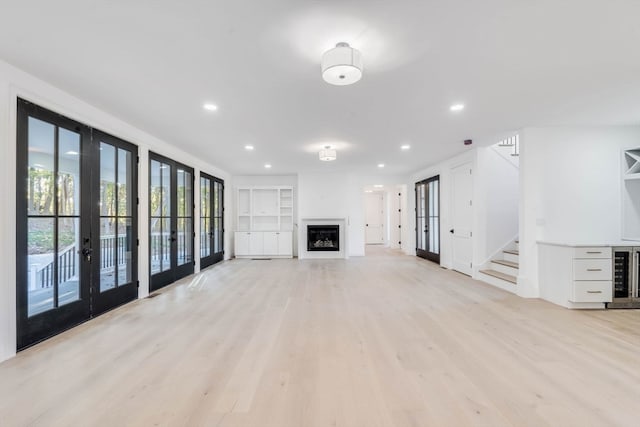 unfurnished living room with light hardwood / wood-style floors, french doors, and beverage cooler