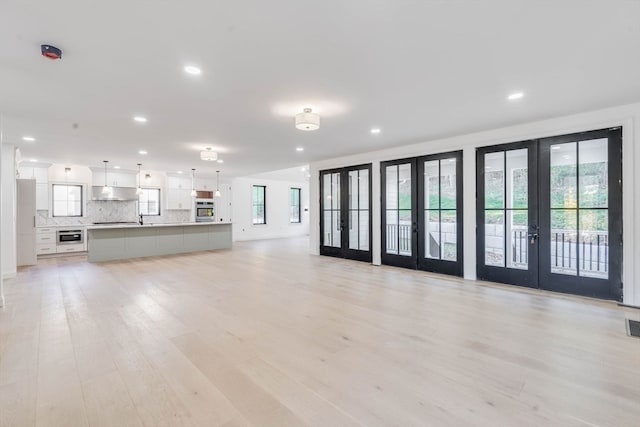 unfurnished living room featuring a wealth of natural light, sink, french doors, and light hardwood / wood-style flooring