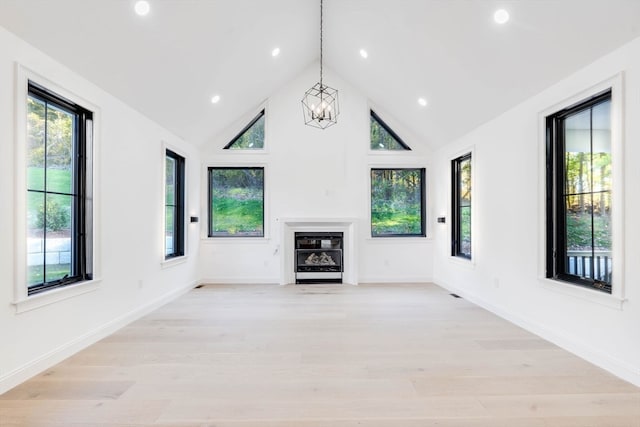 unfurnished living room with light hardwood / wood-style floors, an inviting chandelier, and high vaulted ceiling