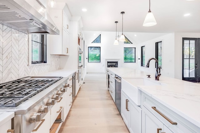 kitchen featuring appliances with stainless steel finishes, wall chimney exhaust hood, white cabinets, and pendant lighting