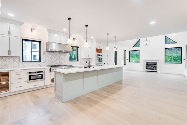 kitchen with a wealth of natural light, pendant lighting, a center island with sink, and white cabinets