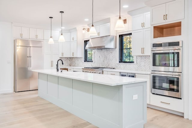 kitchen featuring white cabinetry, light hardwood / wood-style floors, stainless steel appliances, range hood, and a center island with sink