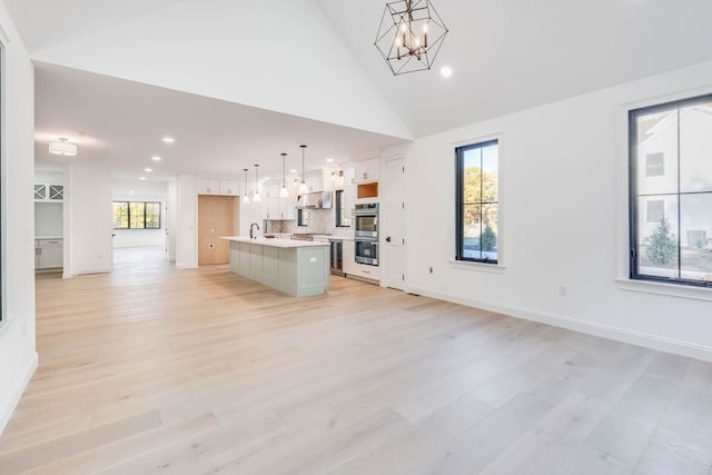 unfurnished living room featuring a chandelier, sink, light hardwood / wood-style floors, and plenty of natural light