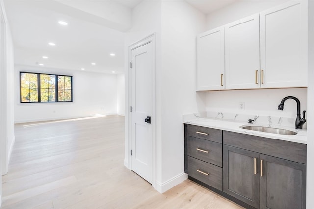 bar with dark brown cabinets, white cabinetry, light stone countertops, light hardwood / wood-style floors, and sink