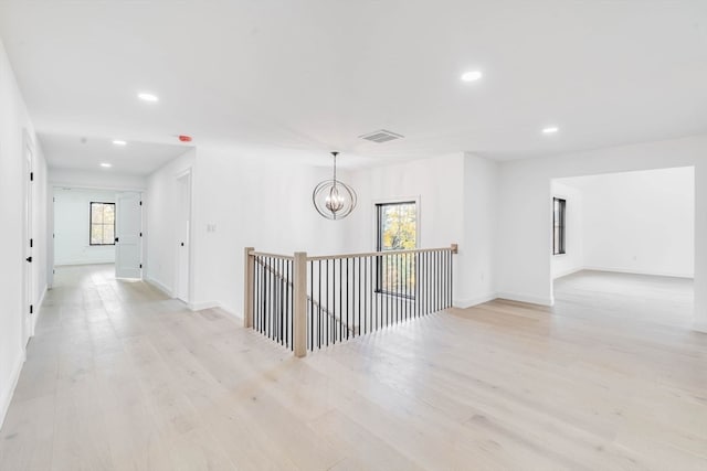 hallway featuring a notable chandelier, light hardwood / wood-style floors, and a healthy amount of sunlight