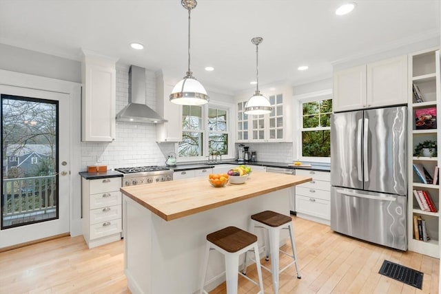 kitchen with wall chimney range hood, wood counters, white cabinetry, visible vents, and stainless steel appliances