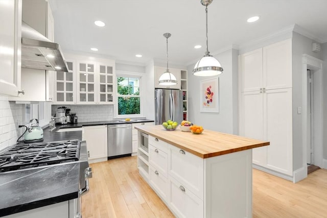kitchen with a sink, wall chimney range hood, appliances with stainless steel finishes, crown molding, and wood counters