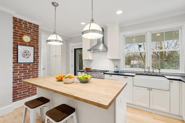 kitchen featuring ornamental molding, light wood-style flooring, white cabinetry, wooden counters, and a sink