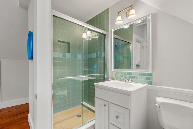 bathroom featuring toilet, a shower stall, vanity, wood finished floors, and backsplash