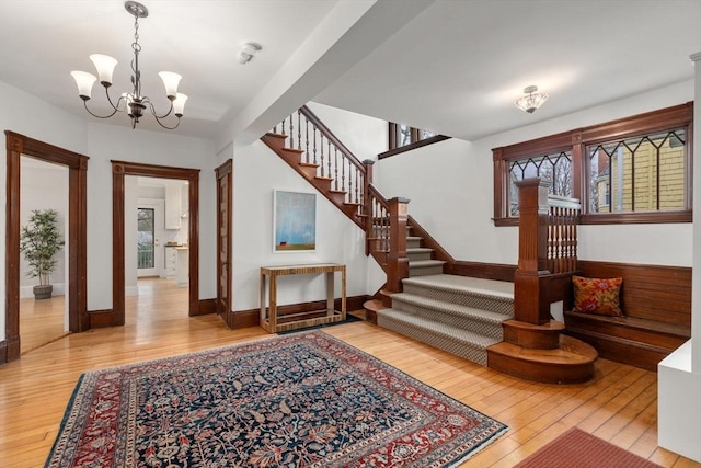foyer featuring baseboards, a notable chandelier, hardwood / wood-style flooring, and stairs