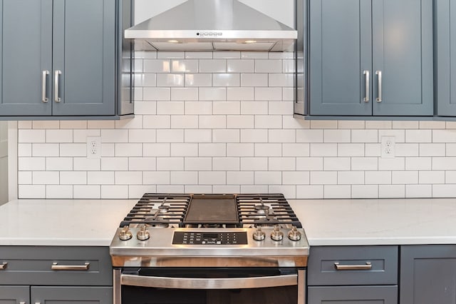 kitchen with gray cabinetry, stainless steel range with gas cooktop, wall chimney range hood, decorative backsplash, and light stone counters