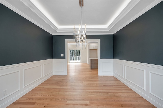 unfurnished dining area featuring a raised ceiling, crown molding, light hardwood / wood-style floors, and a notable chandelier