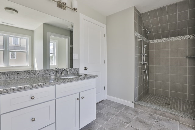 bathroom with tile patterned flooring, a tile shower, and vanity