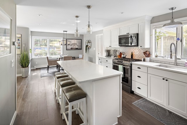 kitchen featuring dark hardwood / wood-style flooring, appliances with stainless steel finishes, a center island, sink, and white cabinets