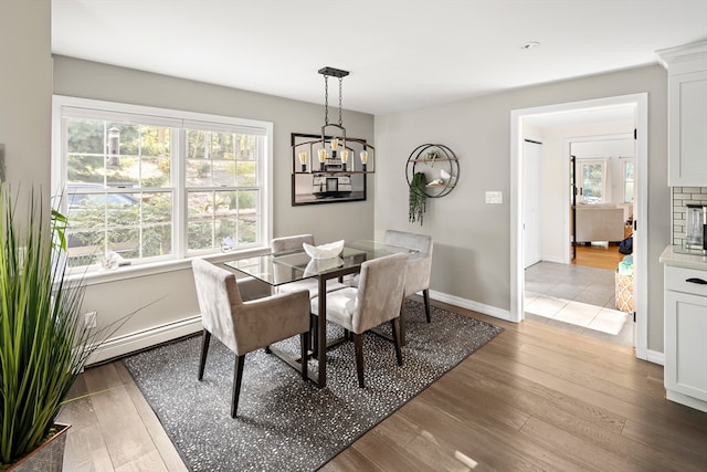 dining area featuring a baseboard radiator, an inviting chandelier, hardwood / wood-style floors, and a fireplace