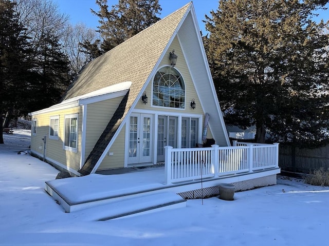 snow covered house with a wooden deck and french doors