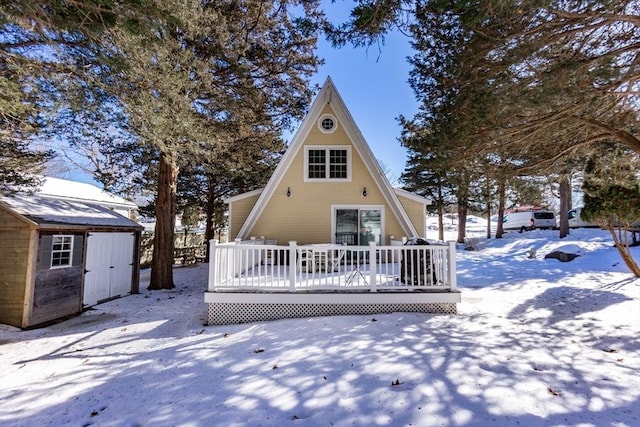 snow covered house featuring a deck and a storage shed