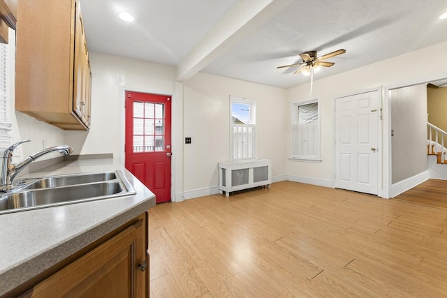 kitchen with radiator heating unit, sink, ceiling fan, beam ceiling, and light hardwood / wood-style flooring