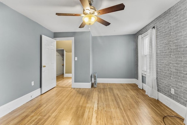 interior space with radiator heating unit, light hardwood / wood-style floors, ceiling fan, and brick wall