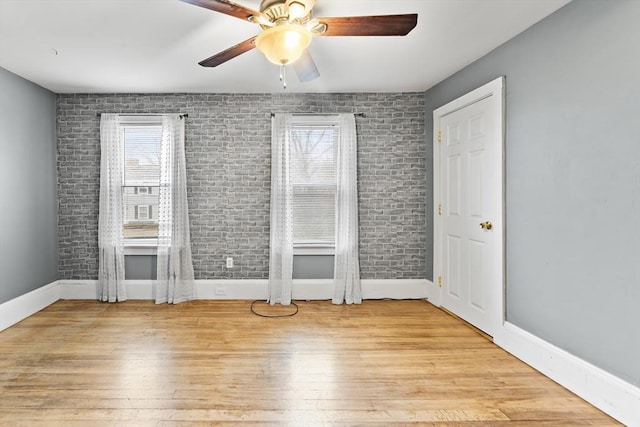 unfurnished bedroom featuring brick wall, light hardwood / wood-style floors, and multiple windows