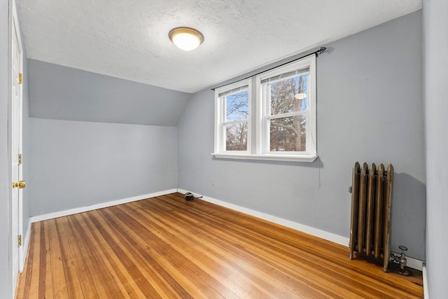 bonus room featuring hardwood / wood-style flooring, radiator, vaulted ceiling, and a textured ceiling