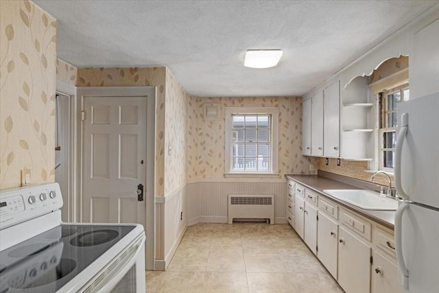 kitchen with white cabinets, radiator heating unit, white appliances, and sink